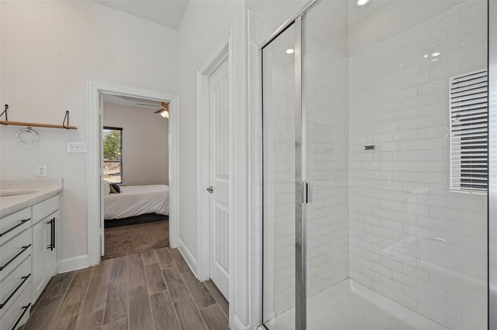 Spacious bathroom featuring wood-look tile flooring, a shower with subway tile surround, and a vanity with a light-toned countertop