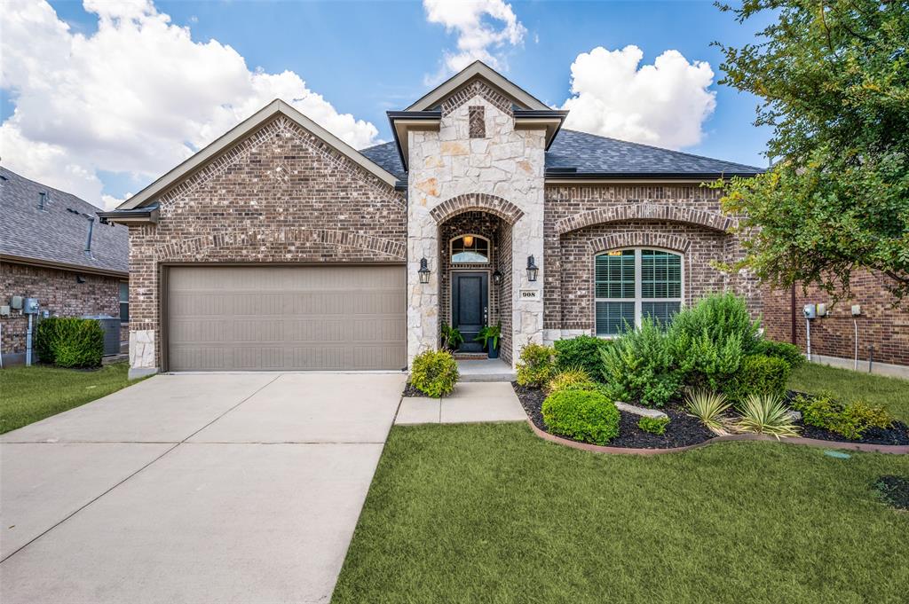 Brick and stone exterior with an arched entryway, mature landscaping, dark-paneled garage door, and a concrete driveway