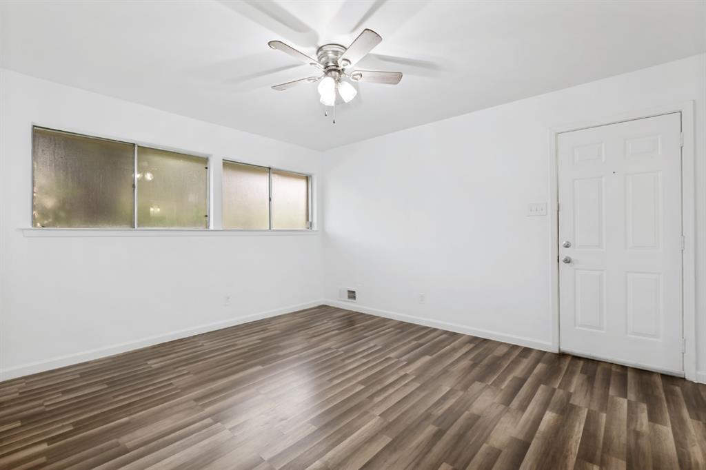 Wood-finish flooring, white walls, multiple windows, white paneled door, and a ceiling fan