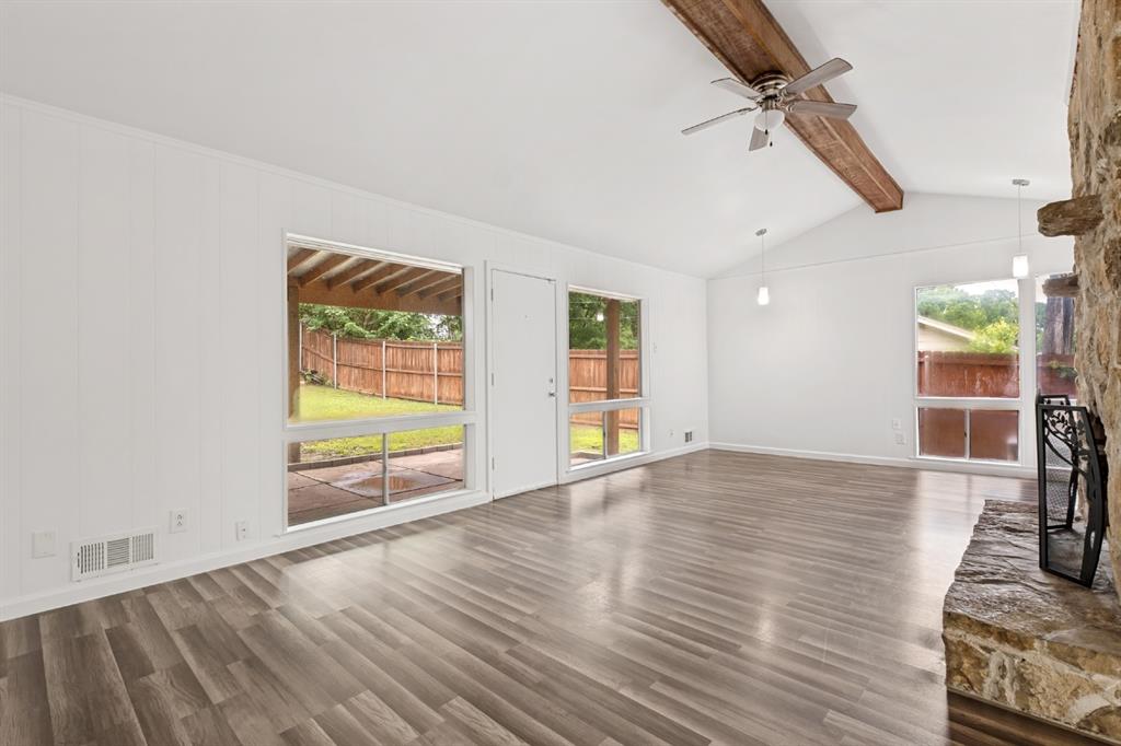 Spacious living area featuring vaulted ceilings, exposed wood beam, a stone-clad fireplace, wood-finish flooring, and multiple windows