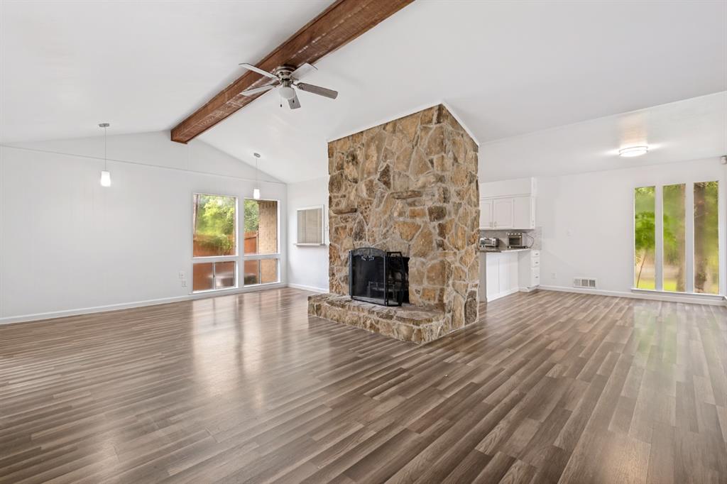 Vaulted ceiling with exposed wood beam, wood-finish flooring, stone-clad fireplace with hearth, built-in kitchen cabinetry