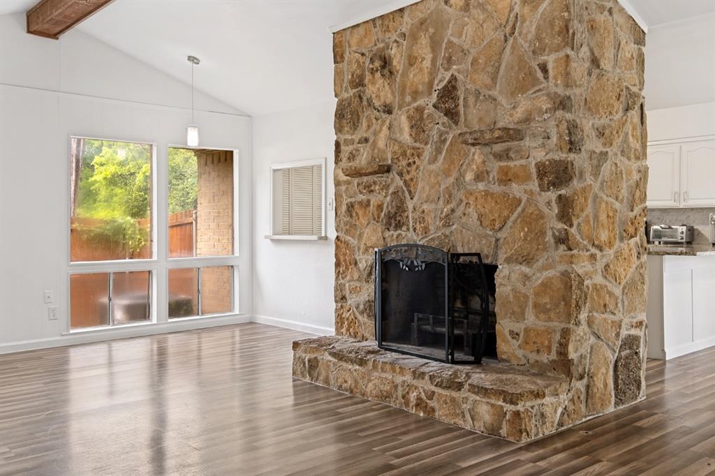 Vaulted ceiling with an exposed beam, stone-clad fireplace with hearth, wood-finish flooring, and large multi-pane windows