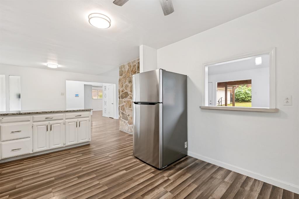 Spacious kitchen featuring white cabinetry with brushed nickel hardware, stainless steel refrigerator, wood-finish flooring, recessed and ceiling-mounted lighting, and a large window providing natural light