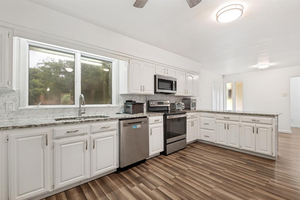 Kitchen featuring white cabinetry, stainless steel appliances, speckled stone countertops, and wood-finish flooring