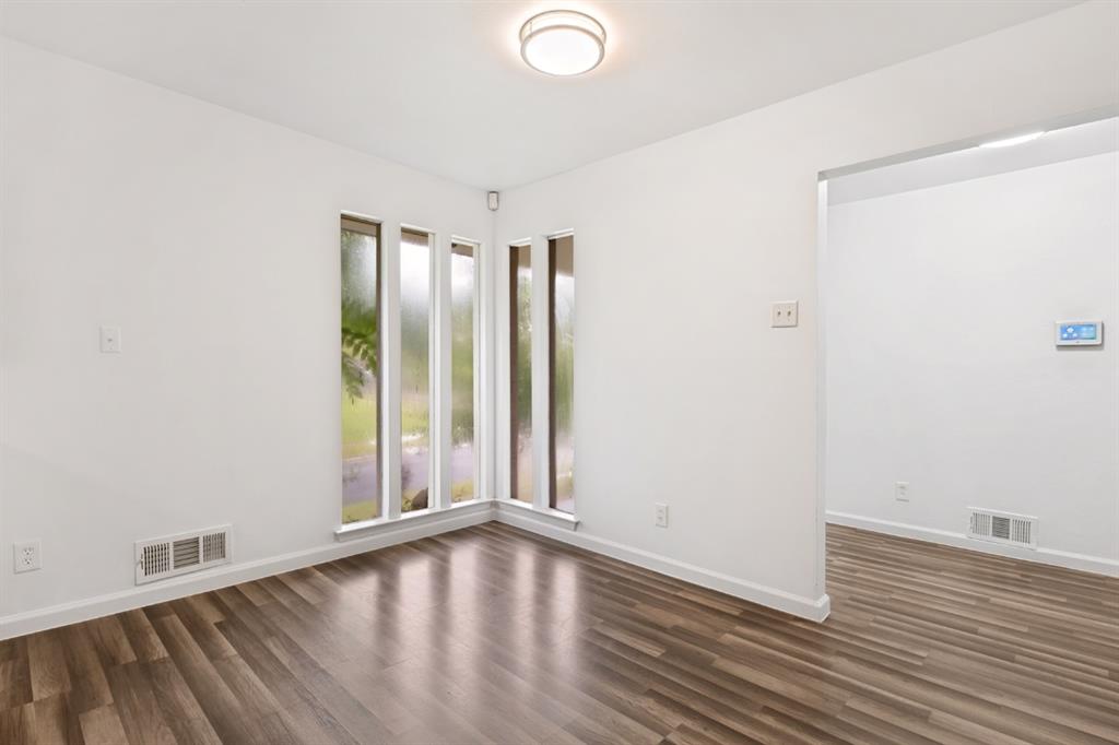 Bright corner room featuring expansive multi-pane windows with natural light, wood-finish flooring throughout, and clean white walls with minimal electrical outlets and light switches visible