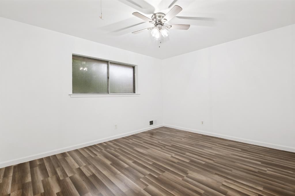 Spacious bedroom showcasing wood-finish flooring with linear plank detailing, white walls, ceiling fan with integrated lighting, and a horizontal window with dual-pane glass providing natural light