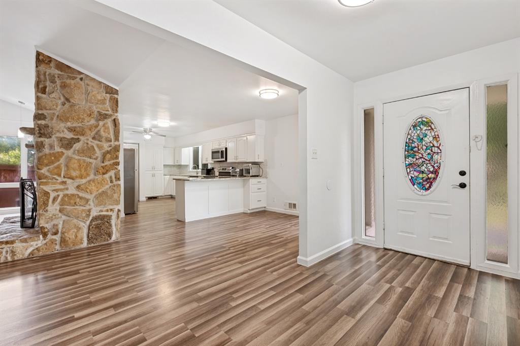 Bright open-concept living area featuring warm wood-finish flooring, stone accent wall, and seamless entry to the kitchen