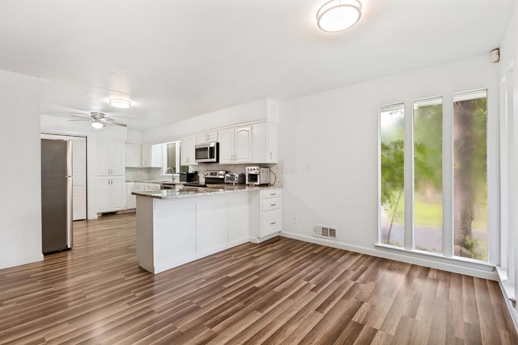 White cabinetry with stainless steel appliances, wood-finish flooring, a kitchen island with a stone countertop, and large vertical windows
