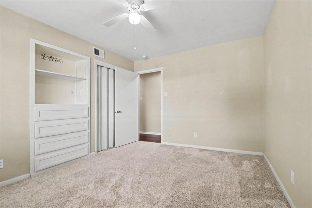Built-in shelving and dresser unit, ceiling fan with light fixture, carpeted flooring, and a sliding closet door