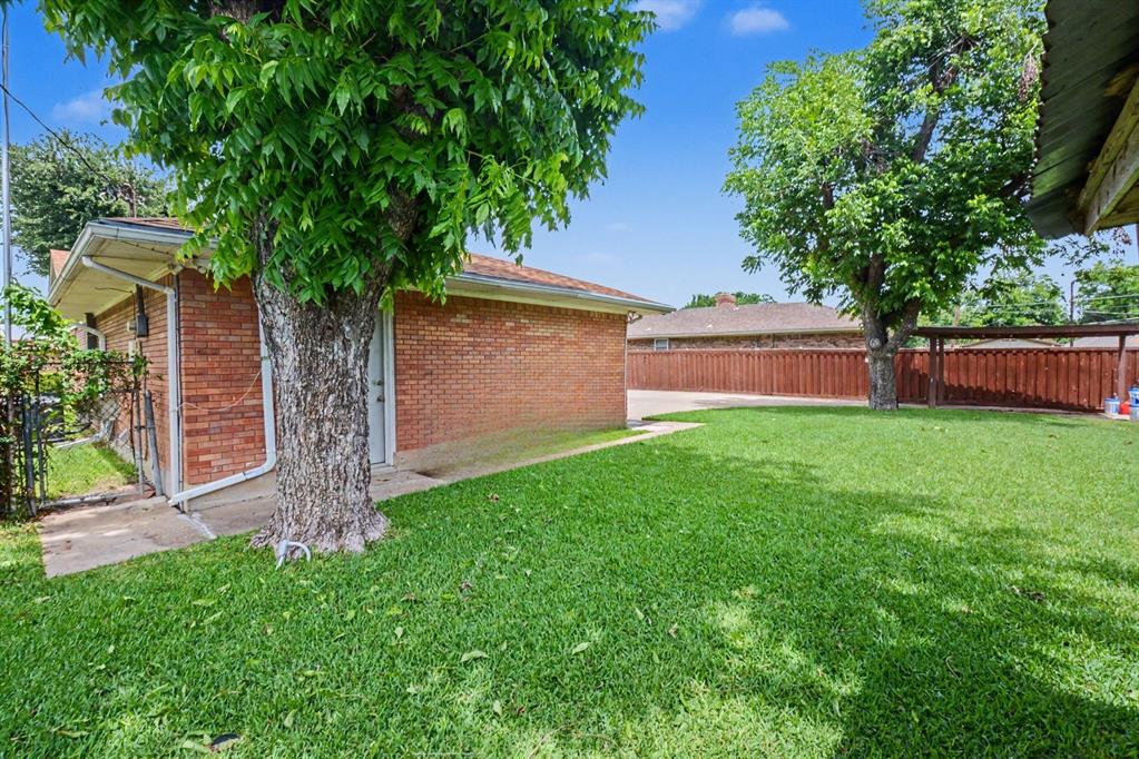 Expansive lawn area with mature trees, brick exterior structure, and wood privacy fencing