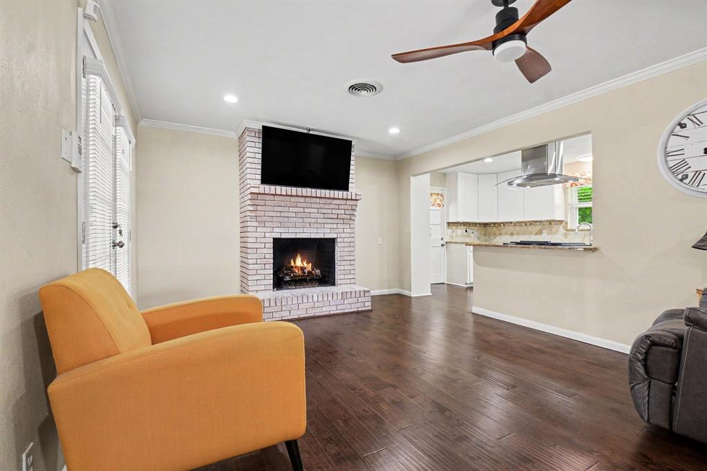 Hardwood flooring, brick fireplace, recessed lighting, ceiling fan, and a kitchen pass-through with stone countertops