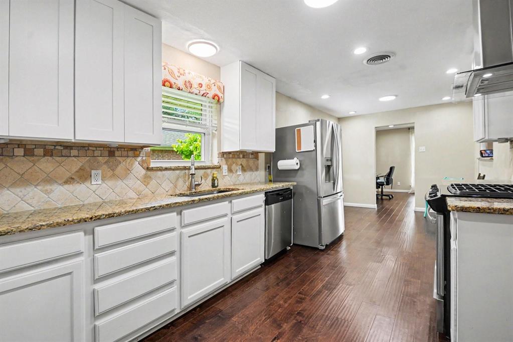 Well-appointed kitchen featuring white cabinetry, granite-style countertops, mosaic tile backsplash, stainless steel appliances, and wood-finish flooring