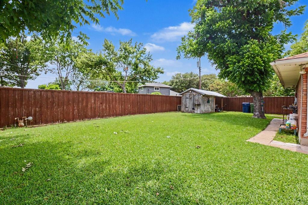Spacious backyard featuring a manicured lawn, a wood privacy fence, mature trees, and a detached storage shed
