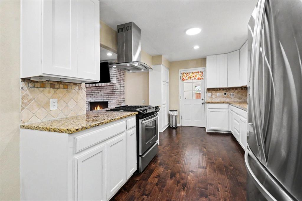 Kitchen featuring white cabinetry, granite countertops, tile backsplash, stainless steel appliances, and wood-finish flooring