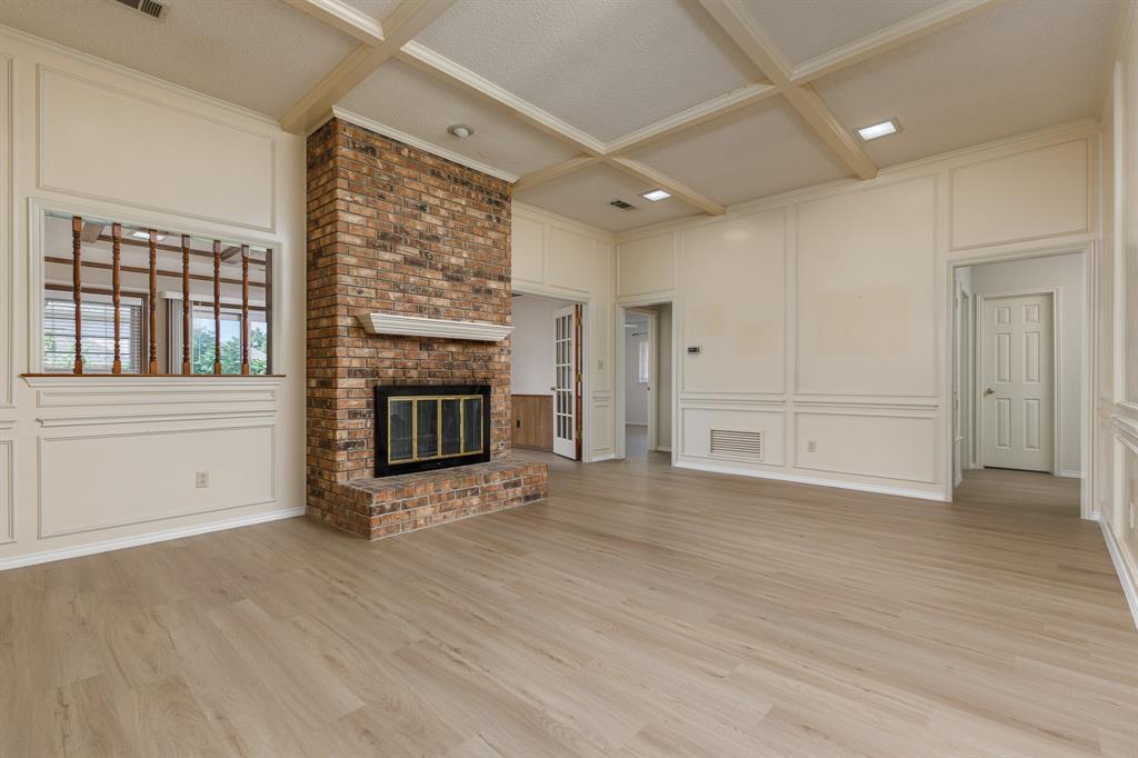 Expansive room featuring a brick fireplace, wood-finish flooring, coffered ceiling, wall paneling, and an interior window with wood detailing