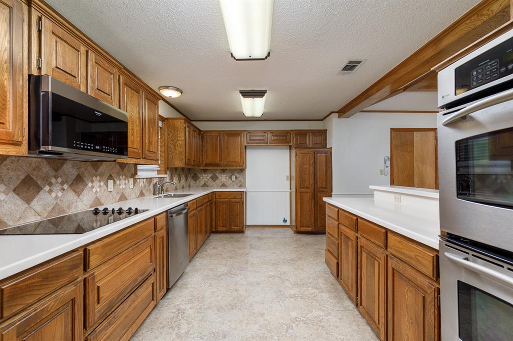 Expansive kitchen featuring wood cabinetry, white countertops, stainless steel appliances, and a tiled backsplash