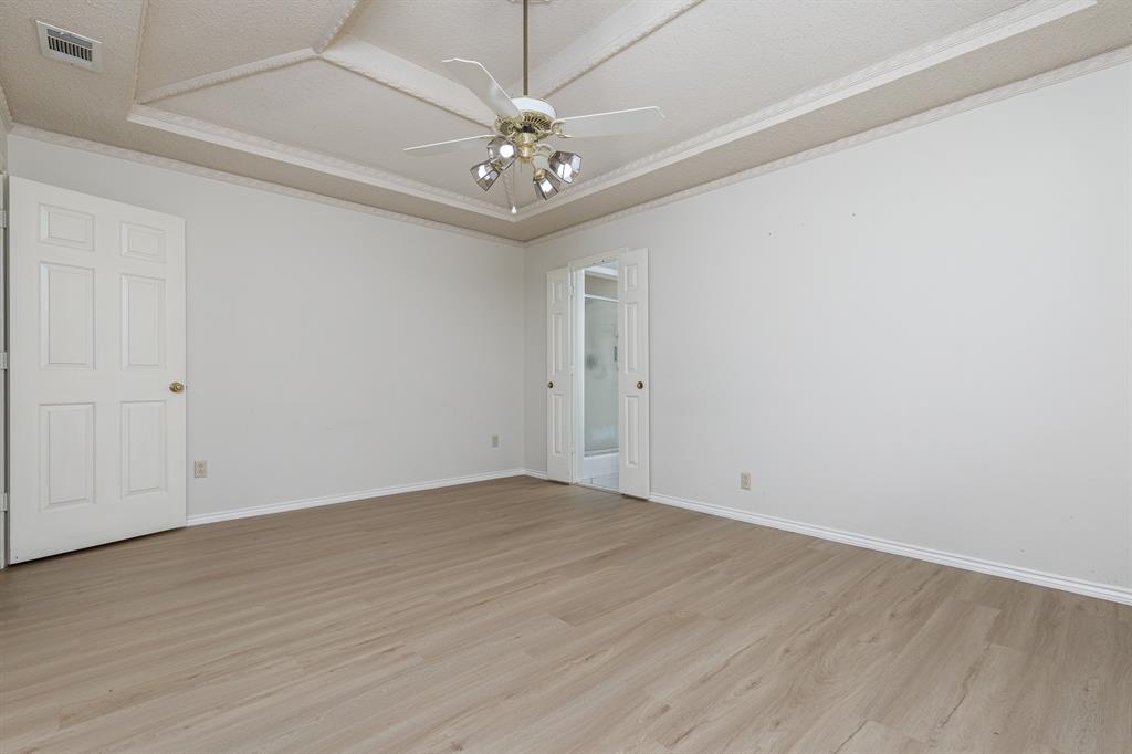 Recessed ceiling with decorative trim, wood-finish flooring, ceiling fan with integrated lighting, and panel doors