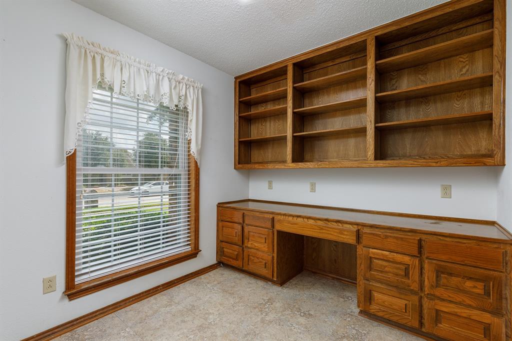 Built-in wood cabinetry with a desk area, overhead wood shelving, and a large window with horizontal blinds