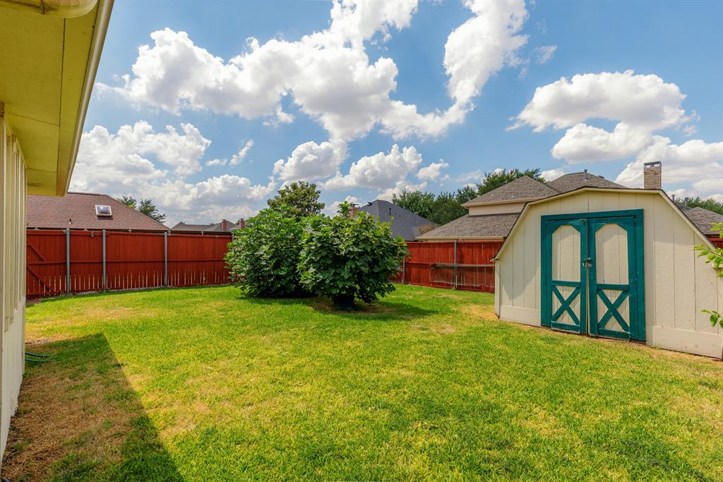Expansive backyard featuring a manicured lawn, established shrubbery, full perimeter fencing, and a detached storage shed