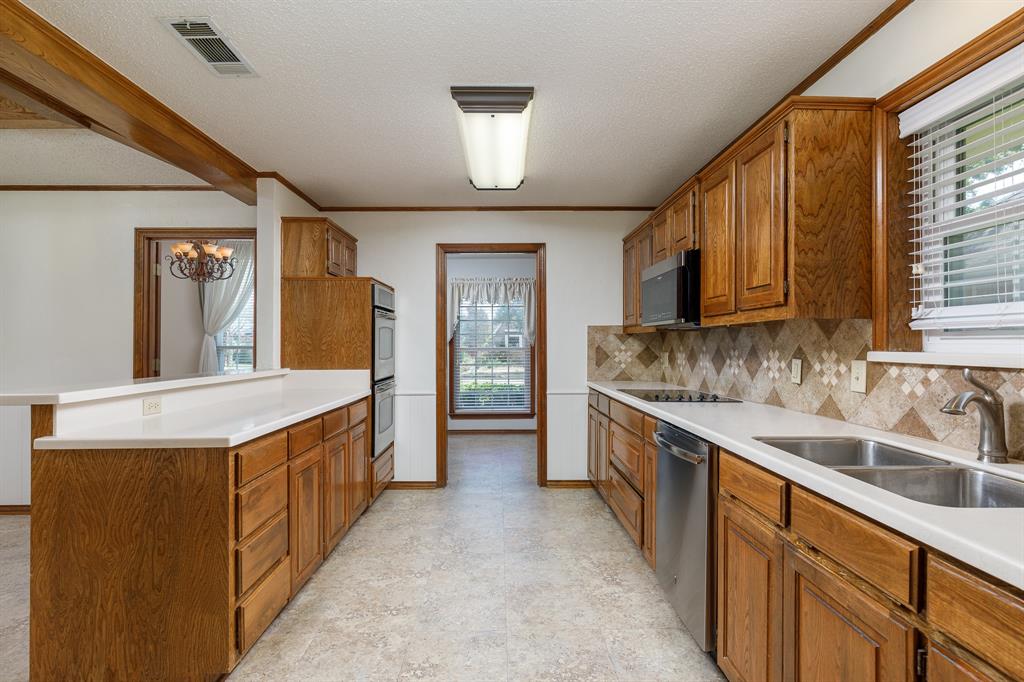 Kitchen featuring natural wood cabinetry, white countertops, built-in stainless steel appliances, patterned tile backsplash, and a double basin sink