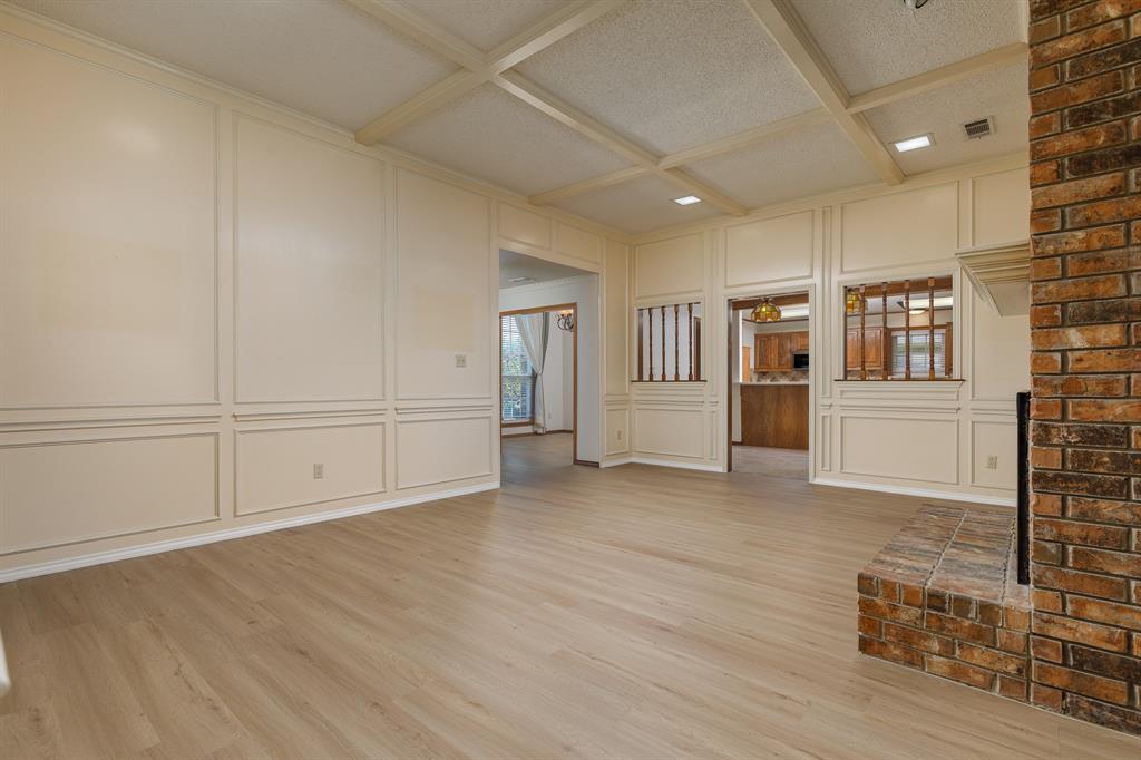 Wood-finish flooring, brick-clad fireplace with hearth, coffered ceiling, and wainscoting paneling