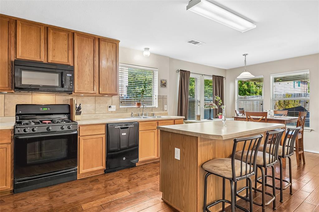 Kitchen featuring wood-finish flooring, wood cabinetry, a center island with countertop seating, and black appliances