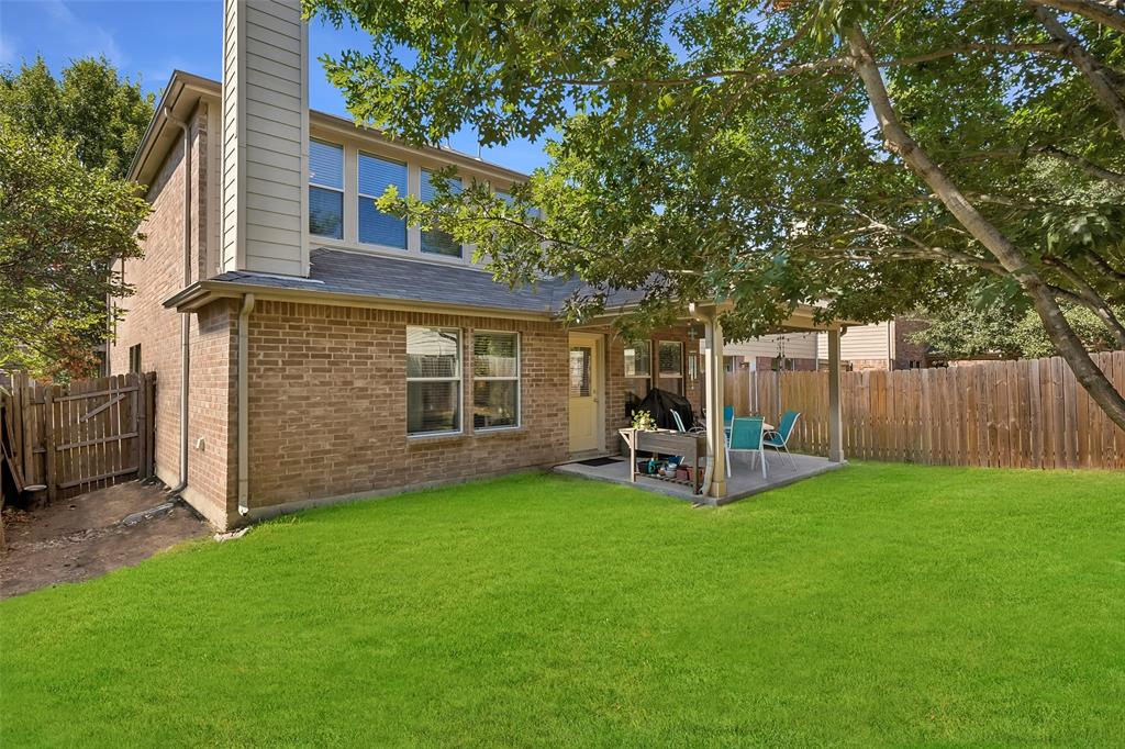 Expansive green lawn with a covered patio, full brick exterior, and a privacy fence