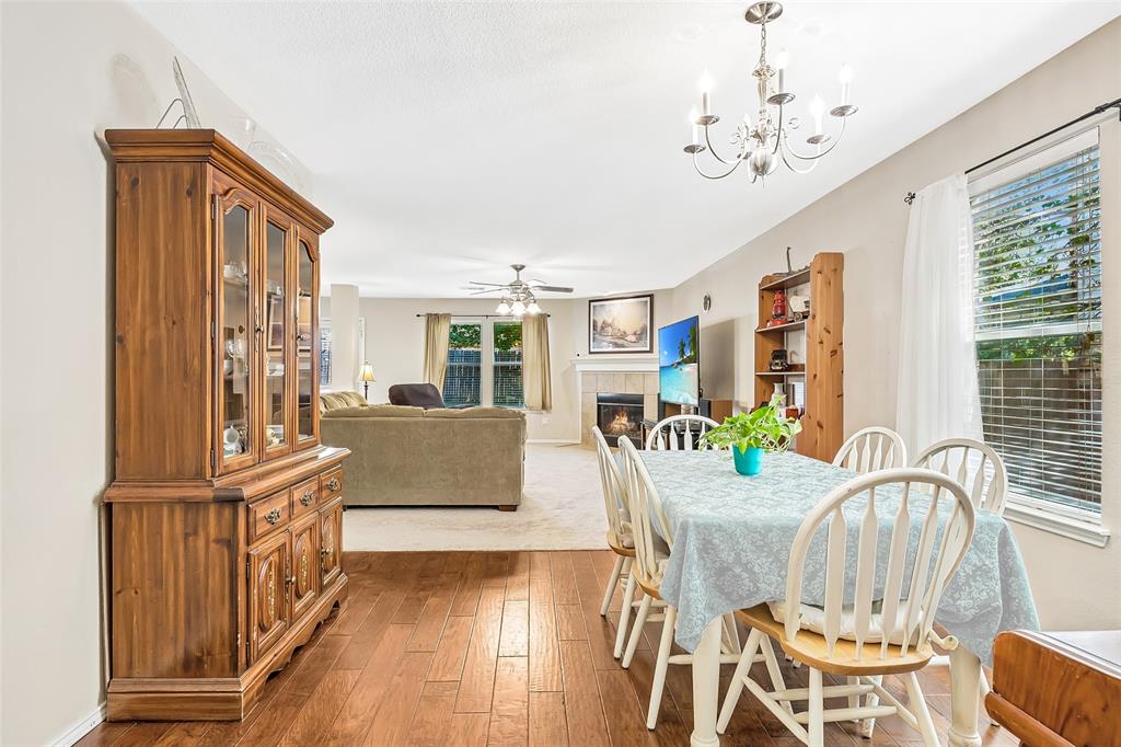 Wood-finish flooring, recessed lighting, and a chandelier illuminate the dining area, which transitions to a living space featuring a fireplace with a mantel Wood-finish flooring, recessed lighting, and a chandelier illuminate the dining area, which transitions to a living space featuring a fireplace with a mantel