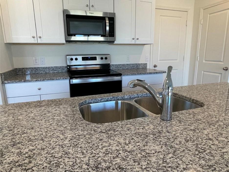 Kitchen featuring granite countertops, stainless steel appliances, white cabinetry, a dual-basin sink, and a pull-down faucet