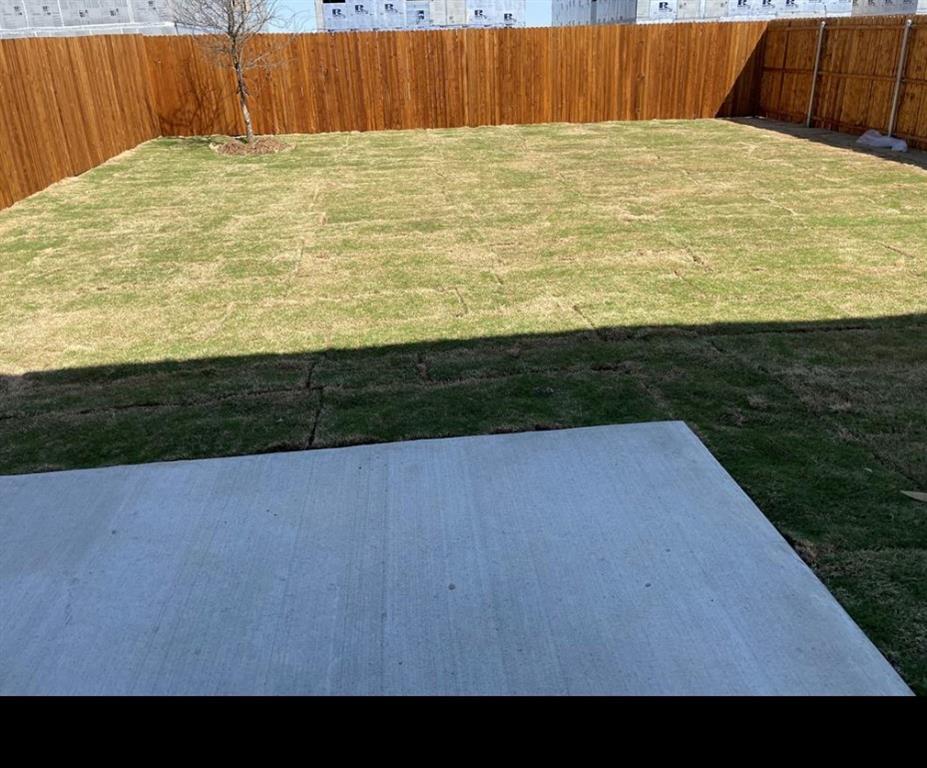 Expansive backyard with a concrete patio, wood privacy fencing, and a mature tree