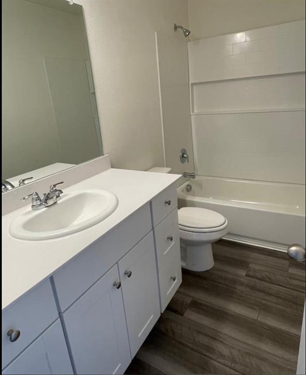 Vanity with an integrated sink and chrome fixtures, white cabinetry with chrome hardware, wood-finish flooring, and a shower-over-tub combination with a subway-tiled surround