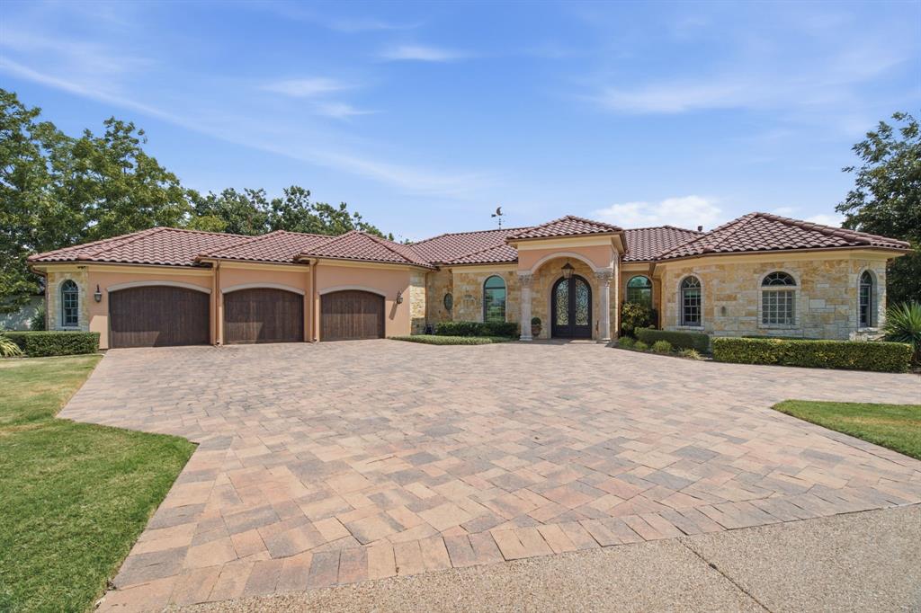 Paver driveway, three-car garage with wood-finish doors, stone facade, arched windows, and a tiled roof Paver driveway, three-car garage with wood-finish doors, stone facade, arched windows, and a tiled roof