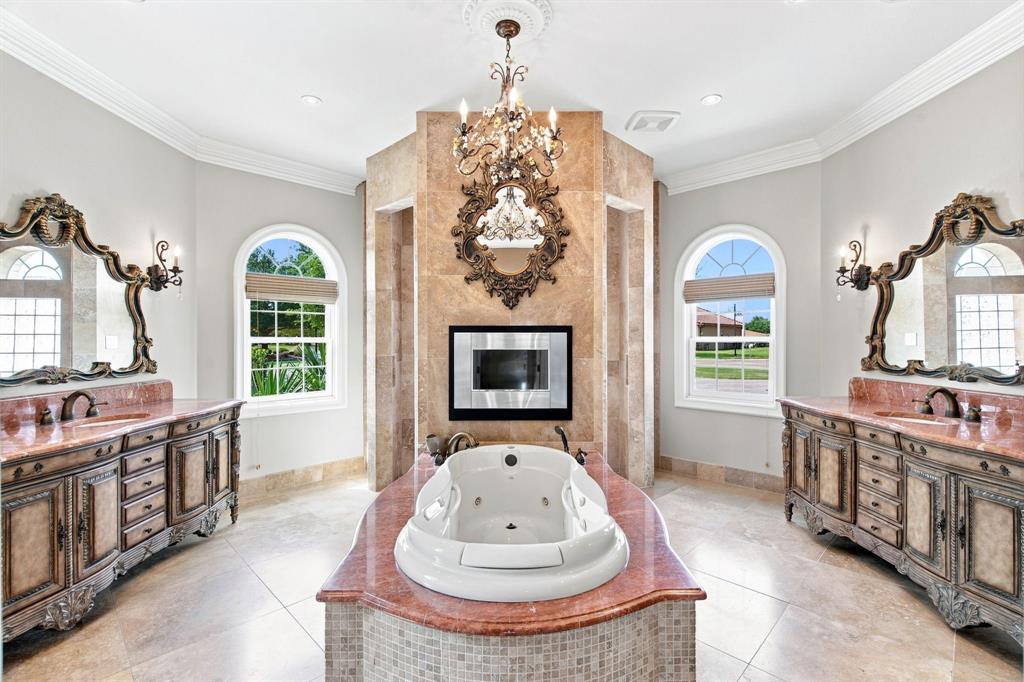 Freestanding soaking tub with a tiled surround, dual vanity stations with ornate mirrors, and arched windows