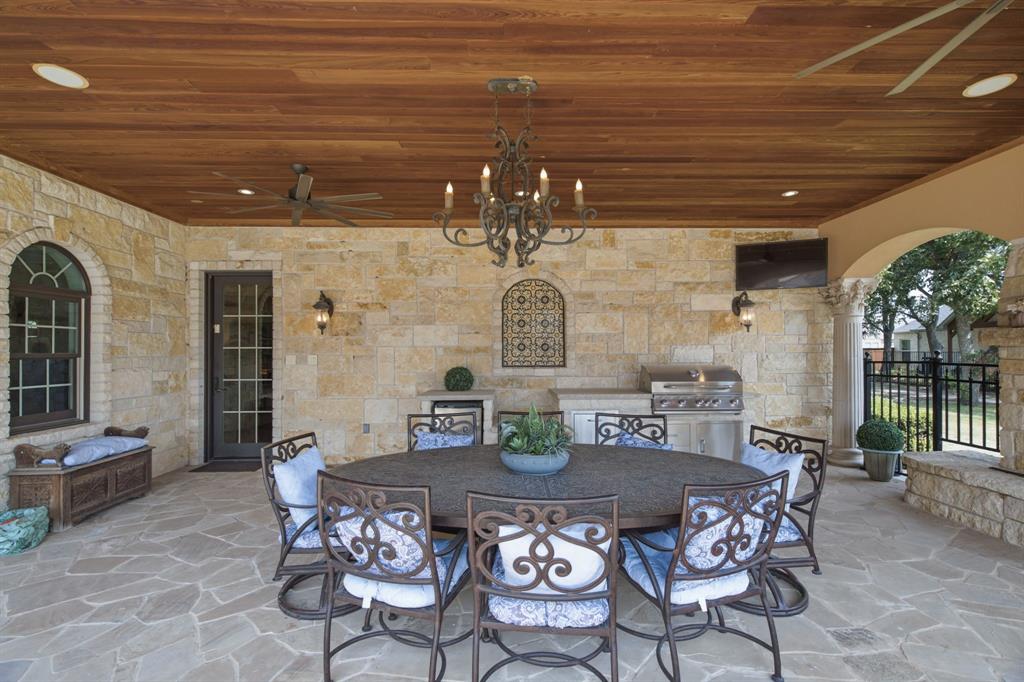 Covered outdoor patio featuring a wood-finish ceiling, stone wall cladding, flagstone flooring, built-in outdoor kitchen with grill, and an arched entryway
