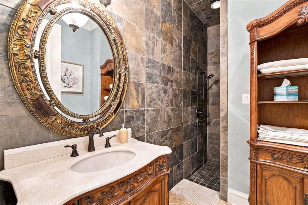 Custom wood-finish vanity with an integrated sink and bronze-tone faucet, ornate framed oval mirror, and a stone-tile shower with a built-in niche