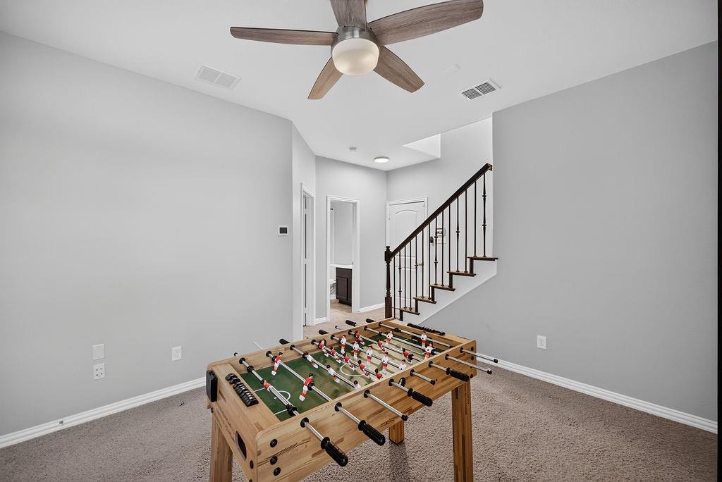 Carpeted area with a ceiling fan, recessed lighting, and a staircase featuring dark wood treads and wrought iron balusters