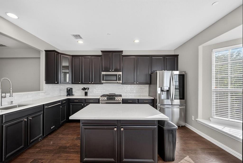 Kitchen featuring dark wood-finish cabinetry, white countertops, white subway tile backsplash, and stainless steel appliances