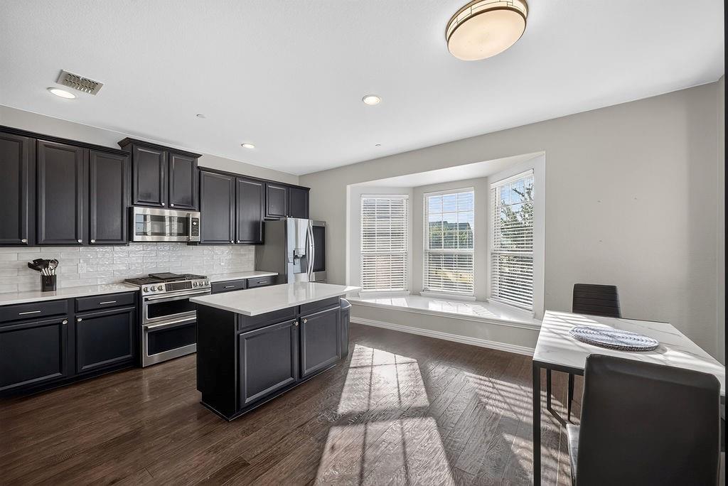 Kitchen with dark cabinetry, stainless steel appliances, a center island with a white countertop, and wood-finish flooring