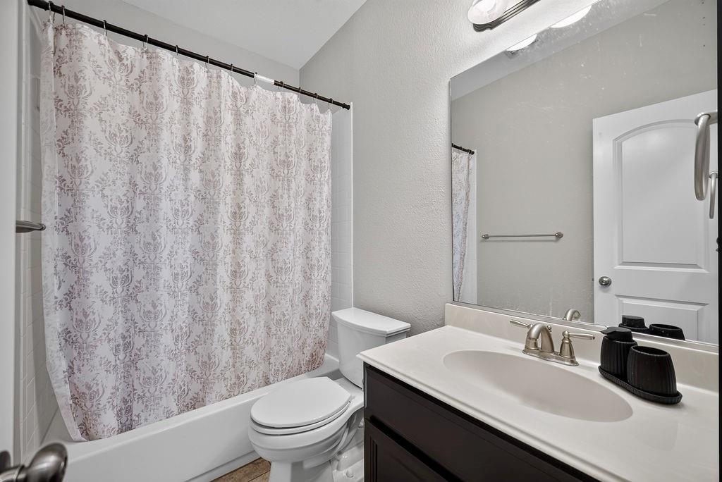 Bathtub with shower, toilet, dark wood-finish vanity with white countertop, integrated sink, and an overhead vanity light fixture