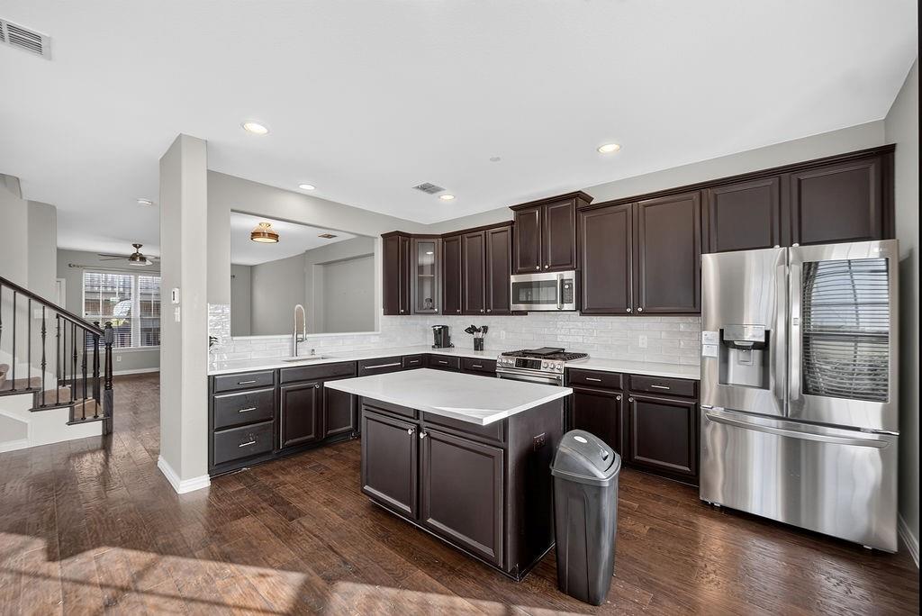 Kitchen featuring dark wood cabinetry, stainless steel appliances, a center island with a white countertop, and wood-finish flooring Kitchen featuring dark wood cabinetry, stainless steel appliances, a center island with a white countertop, and wood-finish flooring