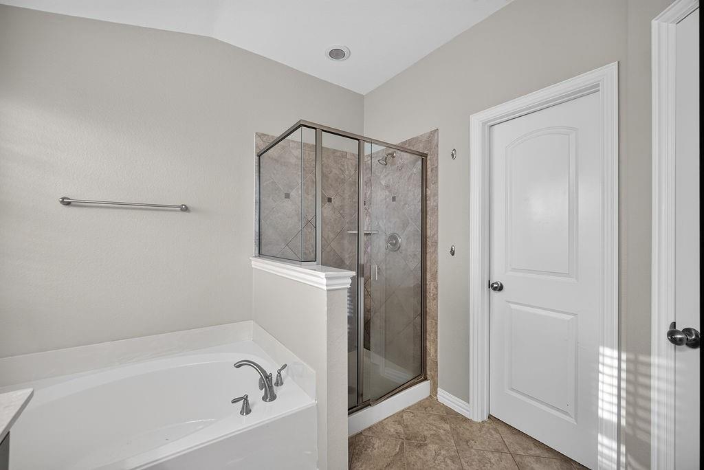 Enclosed glass-panel shower with tiled surround, adjacent soaking tub with deck-mounted faucet, and tile flooring