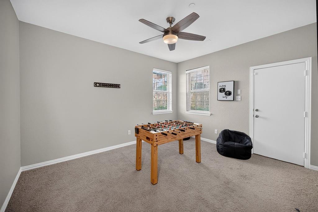 Neutral-toned carpeting, ceiling fan with integrated lighting, two windows with blinds, and a white door with brushed nickel hardware