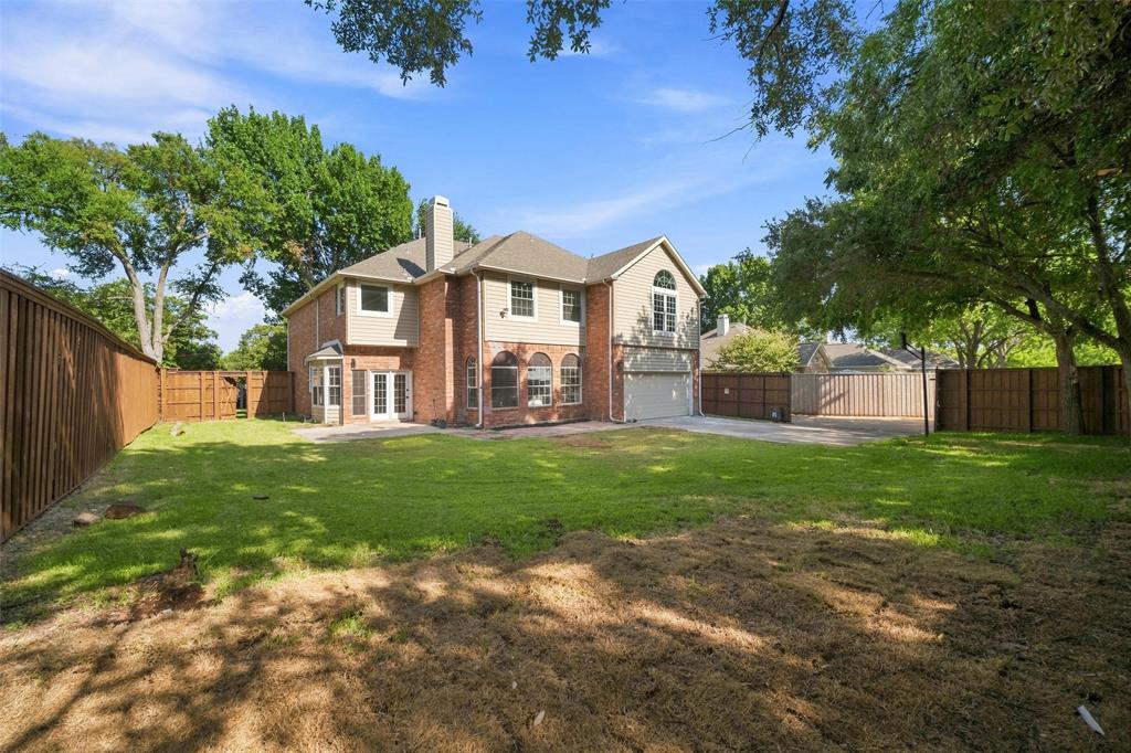 Expansive backyard featuring a manicured lawn, full privacy fencing, mature trees, and a brick and siding exterior
