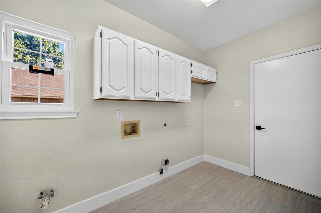 White cabinetry, wood-finish flooring, white door with black hardware, and a window with natural light