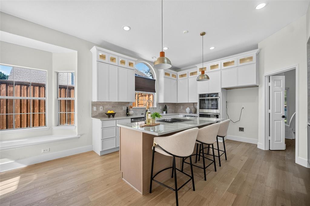 Light wood-finish flooring, white cabinetry with gold-tone accents, an island with countertop seating, a built-in oven, and recessed lighting