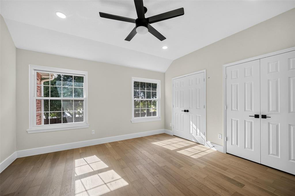 Vaulted ceiling with a ceiling fan, recessed lighting, wood-finish flooring, two double-door closets, and two windows
