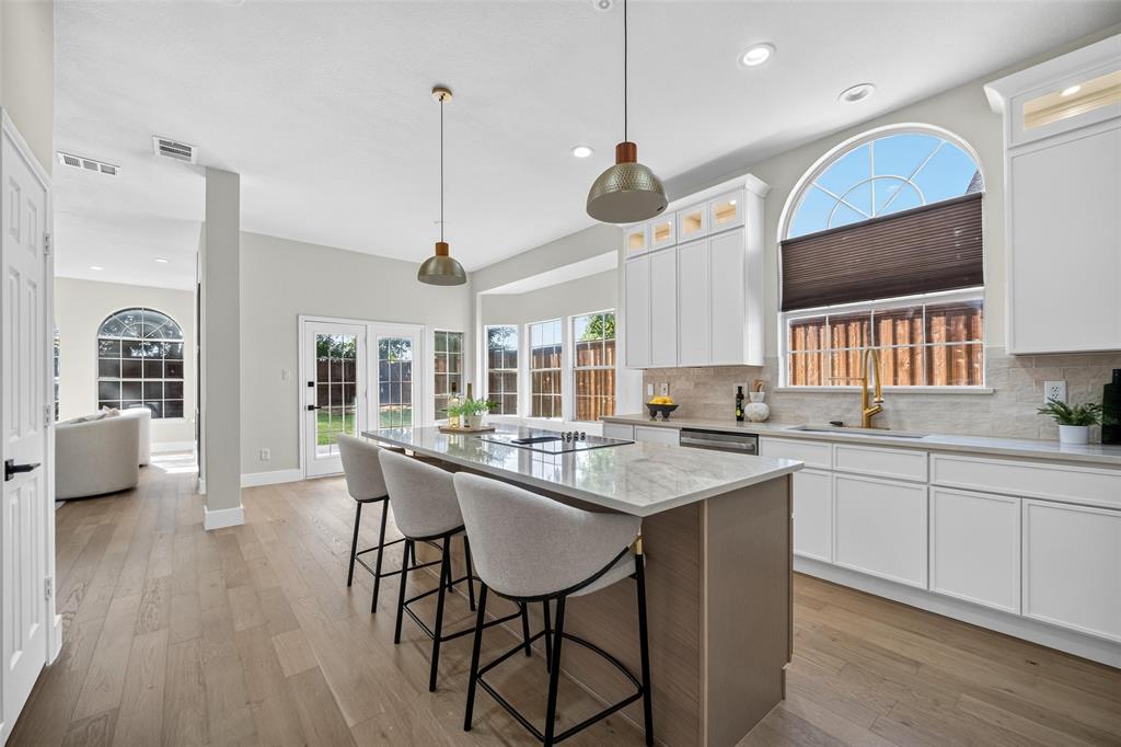 Kitchen with an island featuring a cooktop and stone countertop, white shaker-style cabinetry, wood-finish flooring, and French doors leading to the exterior