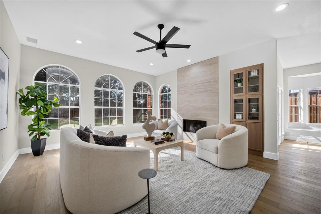 Arch-top windows, wood-finish flooring, recessed lighting, built-in cabinetry with glass doors, and a stone-clad fireplace