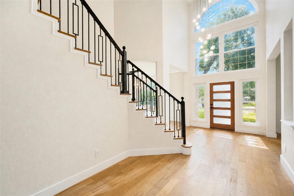 Two-story entryway featuring light wood-finish flooring, a contemporary wood-panel entry door, and a grand staircase with wrought iron balusters and wood treads Two-story entryway featuring light wood-finish flooring, a contemporary wood-panel entry door, and a grand staircase with wrought iron balusters and wood treads