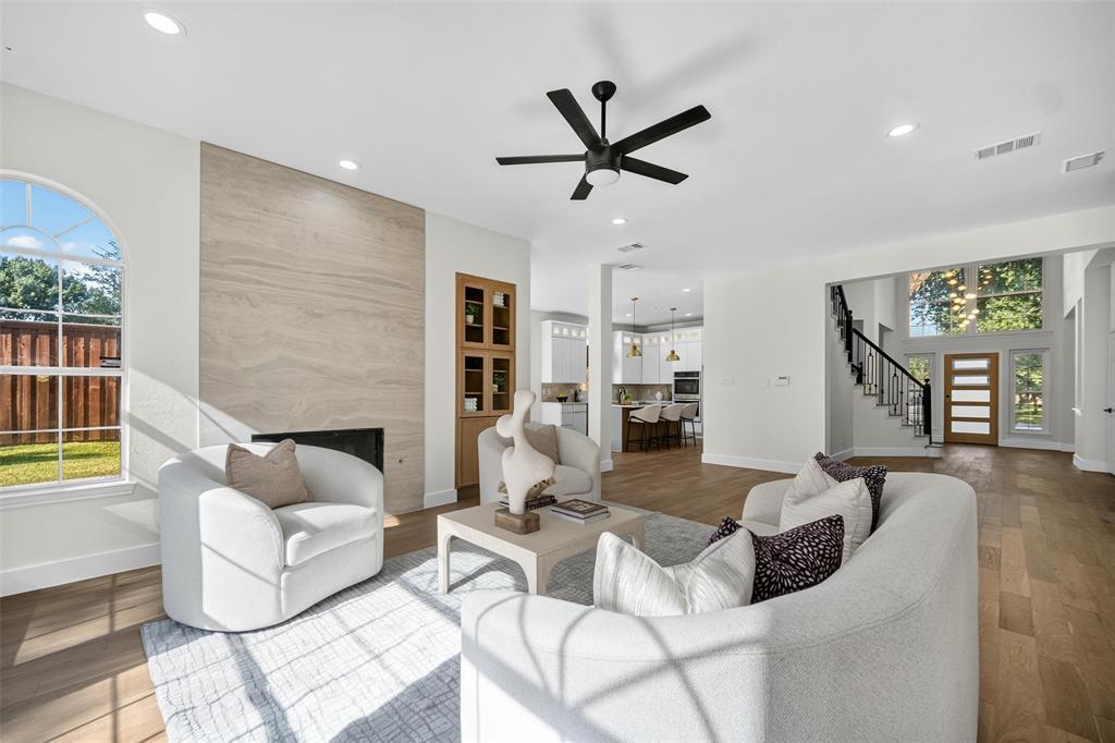 Spacious living area featuring a wood-finish flooring, a contemporary fireplace with a stone surround, recessed lighting, and a modern ceiling fan